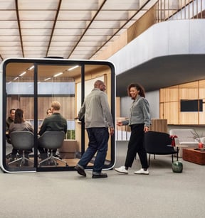 A Framery Six meeting pod in an open atrium, with people walking past